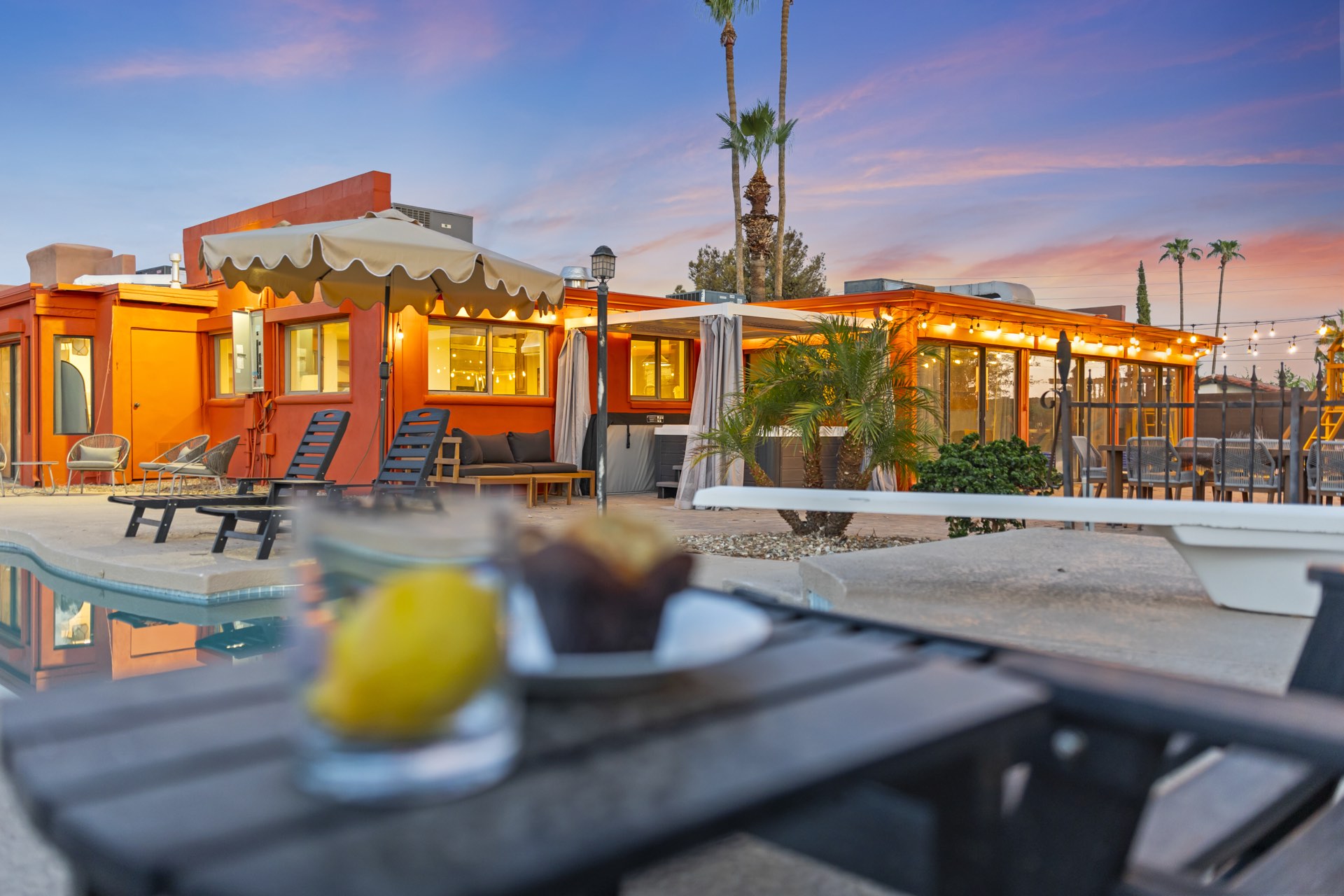 Scottsdale Airbnb at twilight: pool in the foreground, warm light through the glass doors, and a styled table set beside the water.