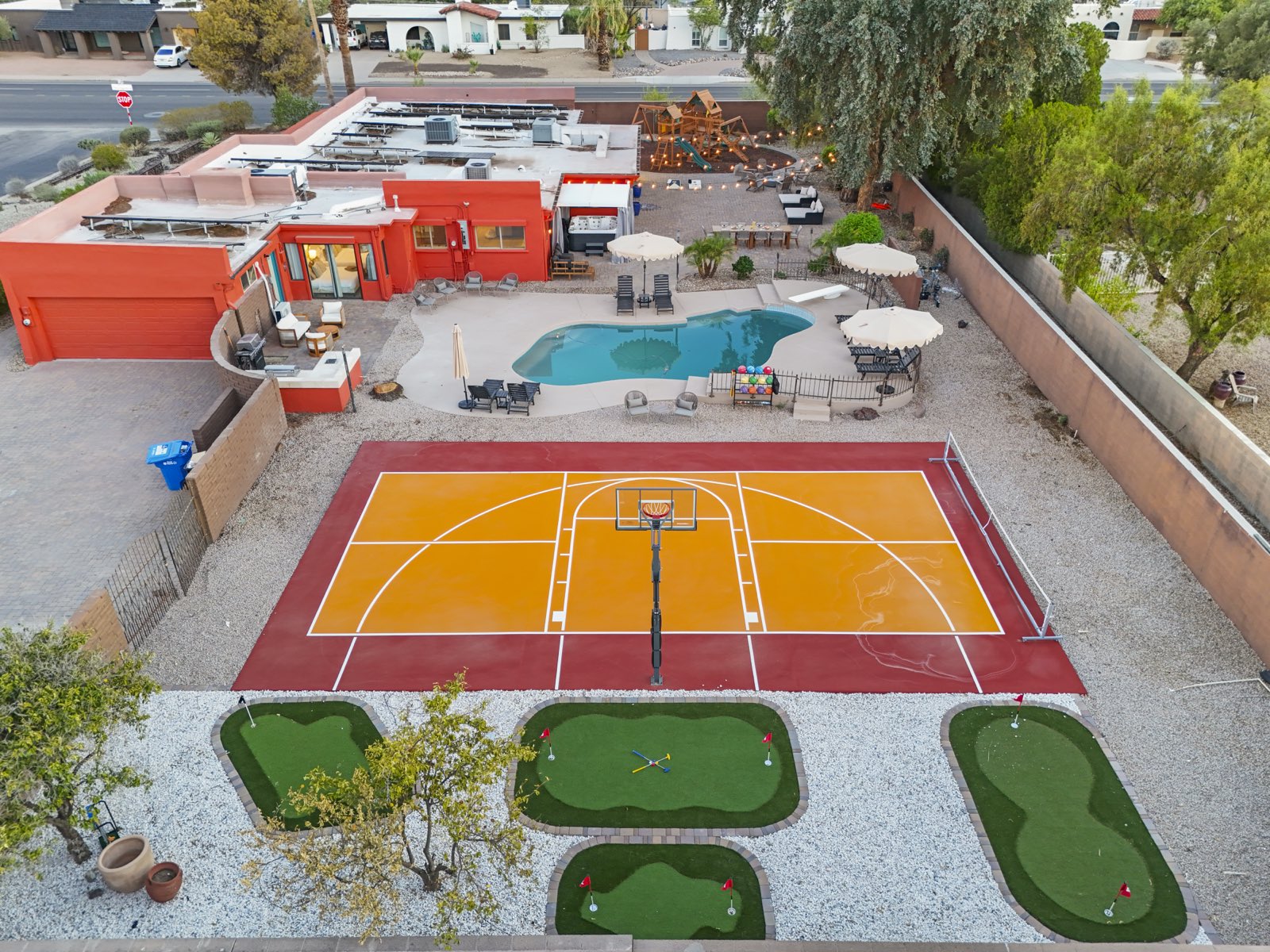 Aerial over a Scottsdale short-term rental at dusk: pool, sport court and putting greens in one frame