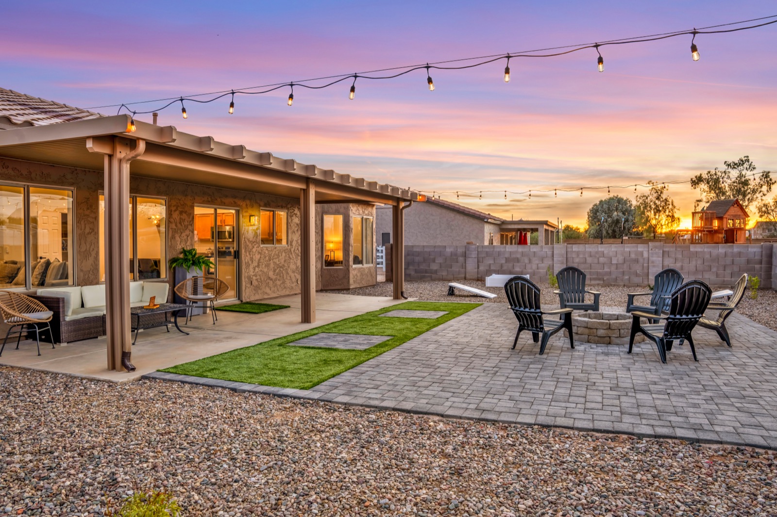 Phoenix Airbnb backyard patio at twilight with string lights, fire pit, and putting green