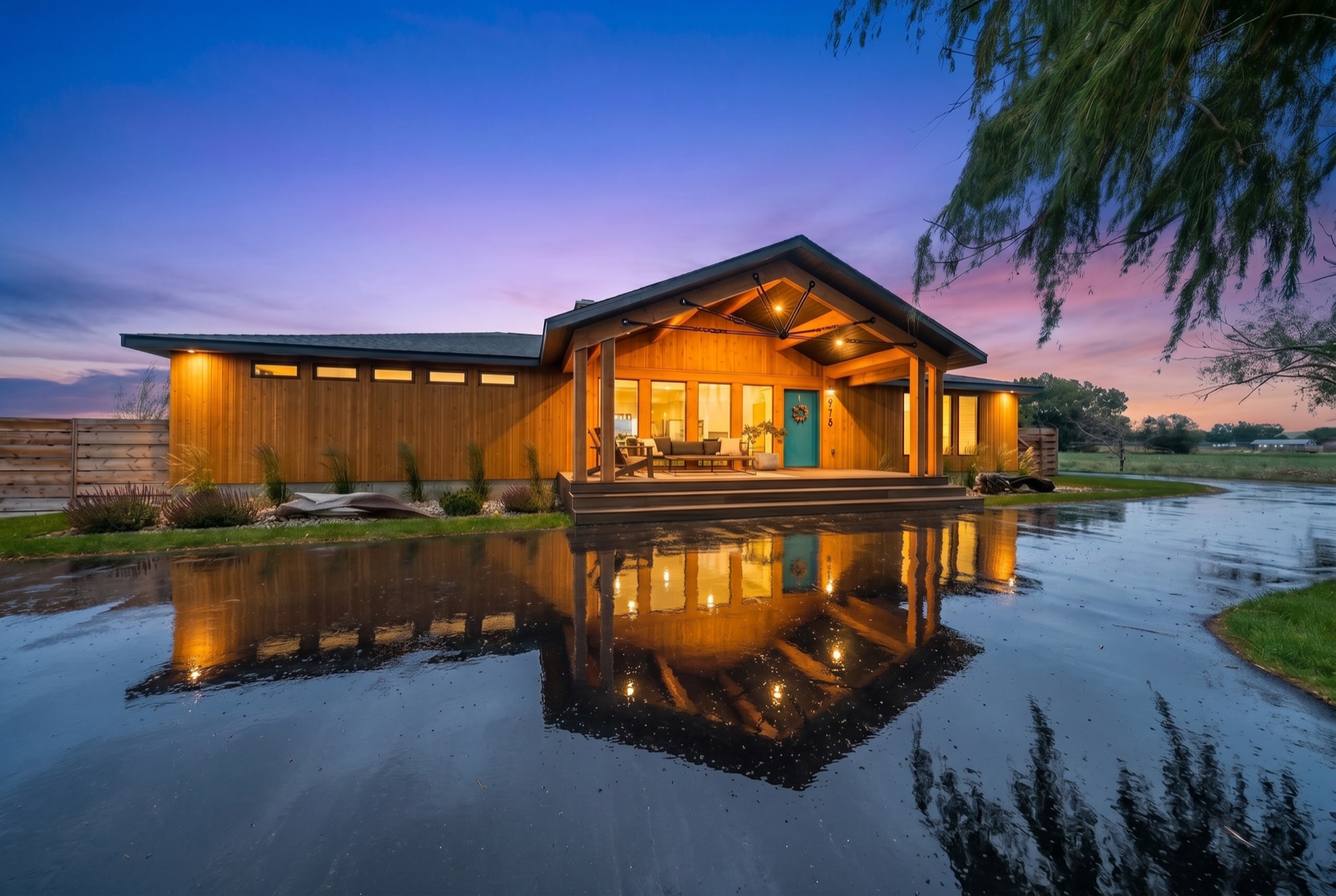 Cedar-clad modern home at twilight with a mirror-like driveway reflection