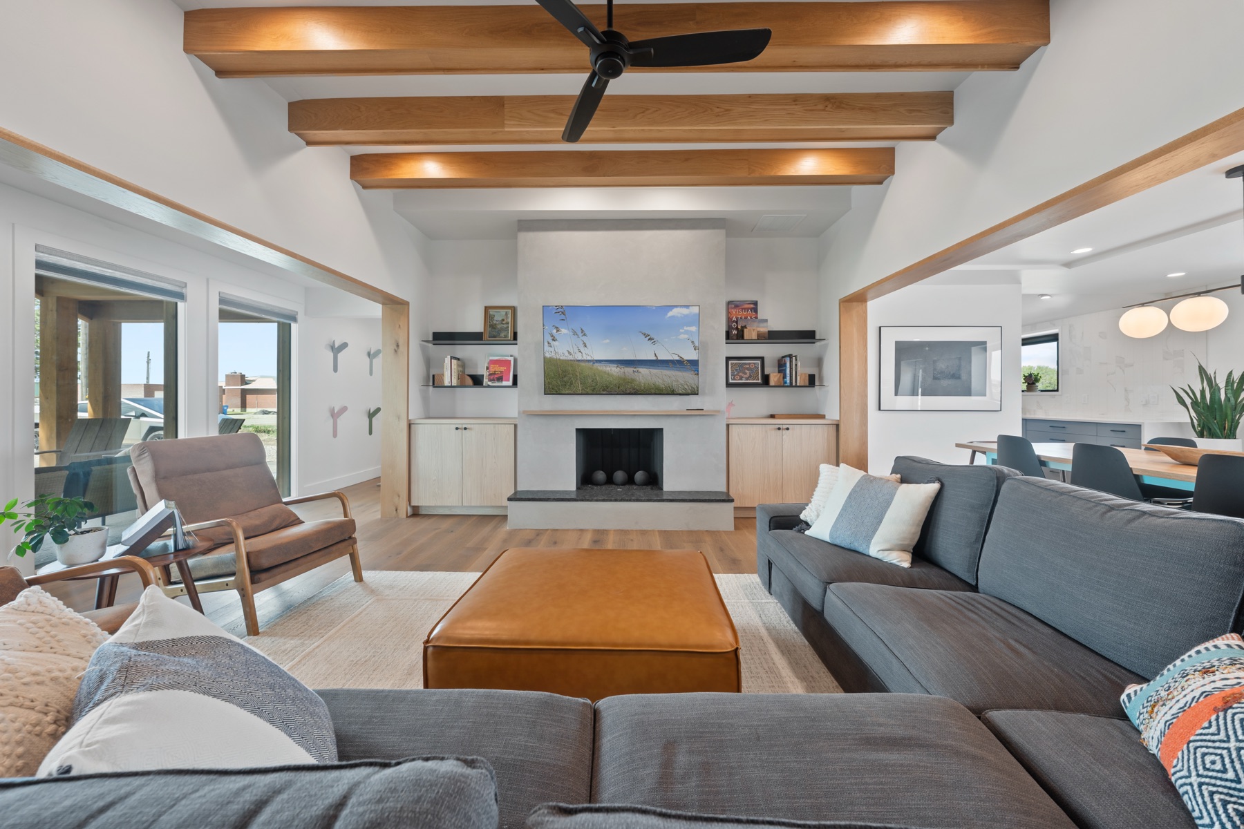 Vaulted timber-beam great room with grey sectional, fireplace, and open-concept dining
